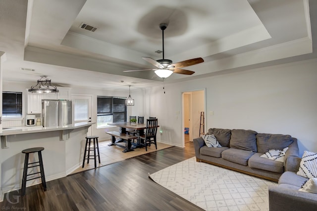 living room with dark hardwood / wood-style flooring, a tray ceiling, ornamental molding, and ceiling fan