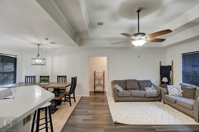 living room featuring a raised ceiling, ornamental molding, hardwood / wood-style flooring, and ceiling fan with notable chandelier