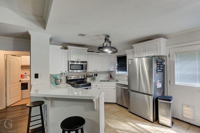 kitchen with a kitchen bar, light tile patterned floors, kitchen peninsula, stainless steel appliances, and white cabinets