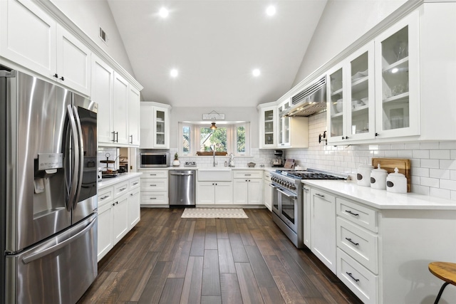 kitchen featuring lofted ceiling, wall chimney range hood, white cabinetry, and appliances with stainless steel finishes