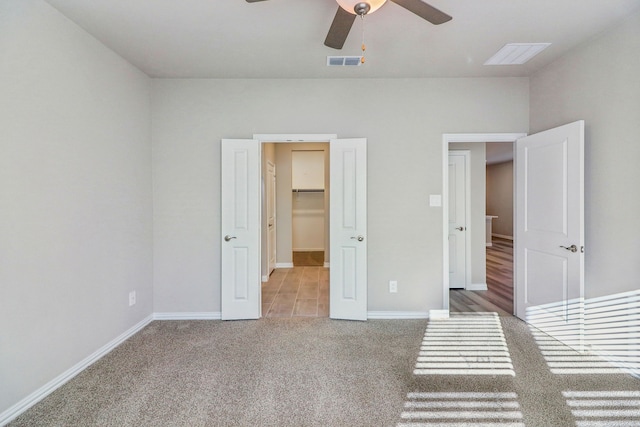 unfurnished bedroom with a spacious closet, light colored carpet, and ceiling fan