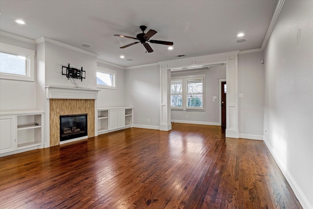 unfurnished living room featuring built in features, a tile fireplace, ceiling fan, ornamental molding, and dark hardwood / wood-style flooring