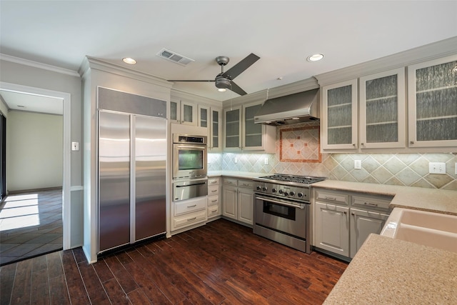 kitchen with high end appliances, ornamental molding, dark hardwood / wood-style floors, decorative backsplash, and wall chimney range hood