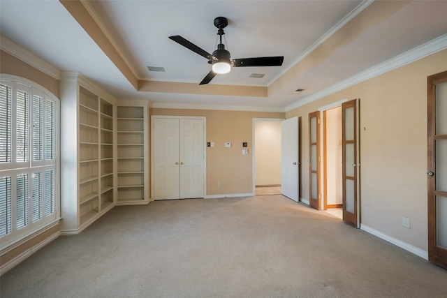 unfurnished bedroom with light carpet, a tray ceiling, crown molding, and ceiling fan