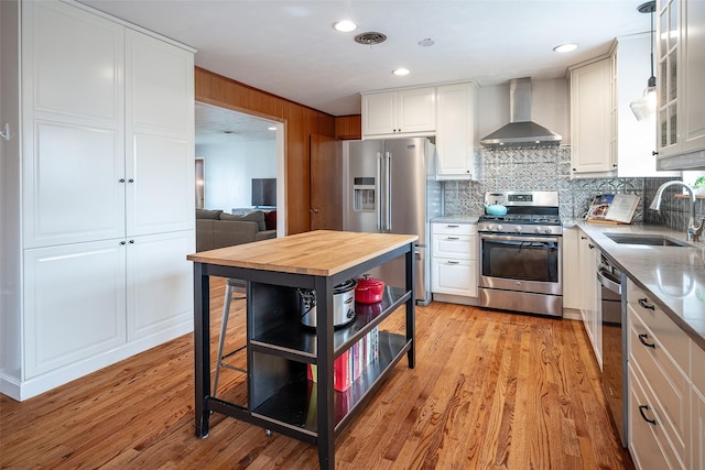 kitchen with sink, decorative light fixtures, appliances with stainless steel finishes, wall chimney range hood, and white cabinets