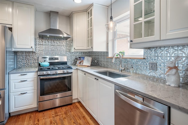 kitchen featuring wall chimney exhaust hood, sink, white cabinetry, decorative light fixtures, and appliances with stainless steel finishes