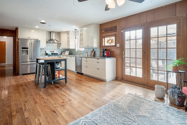 kitchen featuring wall chimney exhaust hood, sink, stainless steel appliances, light hardwood / wood-style floors, and white cabinets