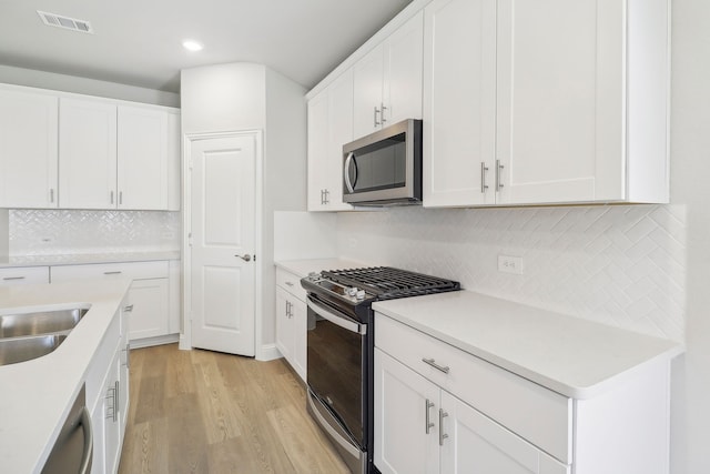 kitchen with white cabinetry, tasteful backsplash, stainless steel appliances, and light hardwood / wood-style flooring