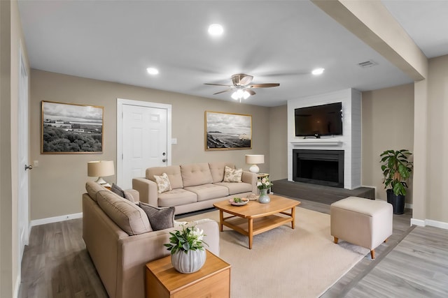 living room with ceiling fan, a large fireplace, and light wood-type flooring