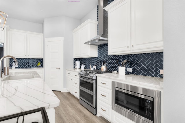 kitchen with wall chimney range hood, sink, white cabinetry, stainless steel appliances, and tasteful backsplash