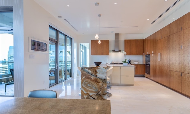 kitchen featuring pendant lighting, double wall oven, a center island, light tile patterned floors, and wall chimney range hood