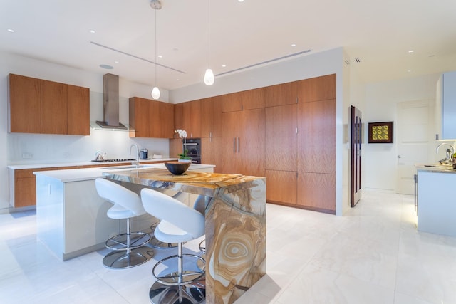 kitchen featuring decorative light fixtures, sink, a kitchen breakfast bar, a large island, and wall chimney exhaust hood