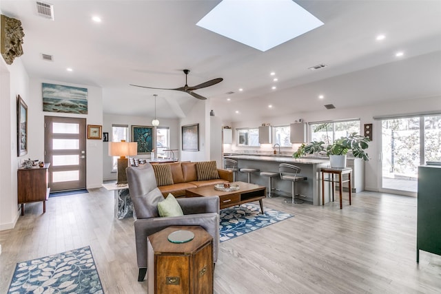 living room featuring ceiling fan, vaulted ceiling with skylight, sink, and light hardwood / wood-style flooring