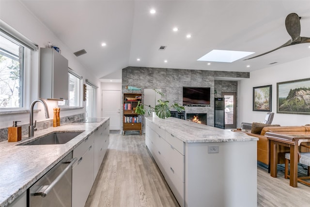 kitchen featuring sink, a large fireplace, stainless steel dishwasher, light wood-type flooring, and a spacious island