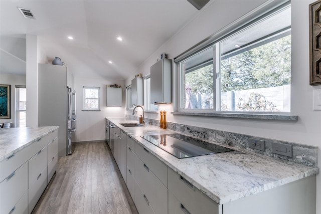 kitchen featuring lofted ceiling, sink, light stone counters, light hardwood / wood-style flooring, and black electric stovetop