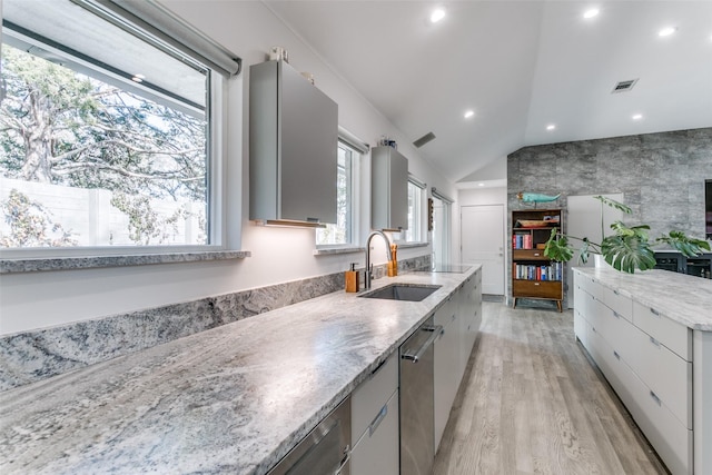 kitchen with lofted ceiling, sink, light stone countertops, stainless steel dishwasher, and light wood-type flooring