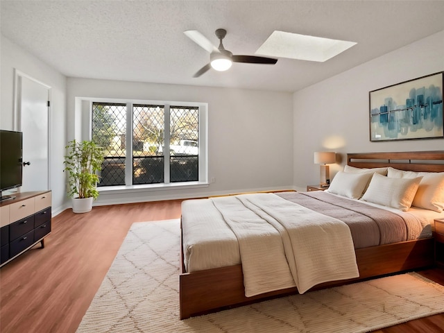 bedroom with light wood-type flooring, a textured ceiling, ceiling fan, and a skylight