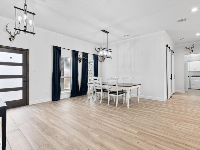 unfurnished dining area featuring washer / clothes dryer, a notable chandelier, crown molding, a barn door, and light wood-type flooring