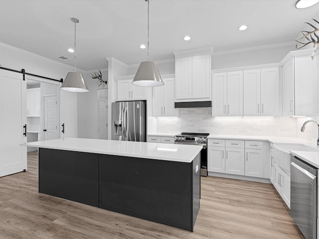 kitchen with appliances with stainless steel finishes, white cabinets, a kitchen island, decorative light fixtures, and a barn door