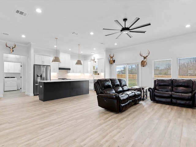 living room with washer / dryer, light hardwood / wood-style flooring, ornamental molding, and ceiling fan