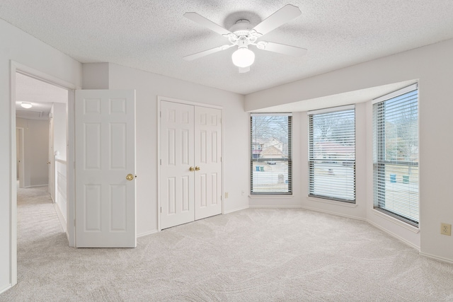 unfurnished bedroom with ceiling fan, light colored carpet, a textured ceiling, and a closet