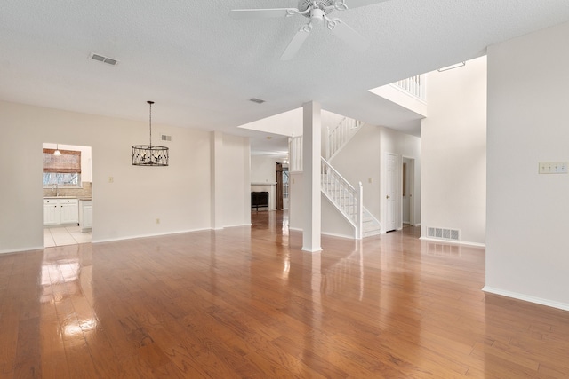 unfurnished living room featuring ceiling fan with notable chandelier, light hardwood / wood-style flooring, and a textured ceiling