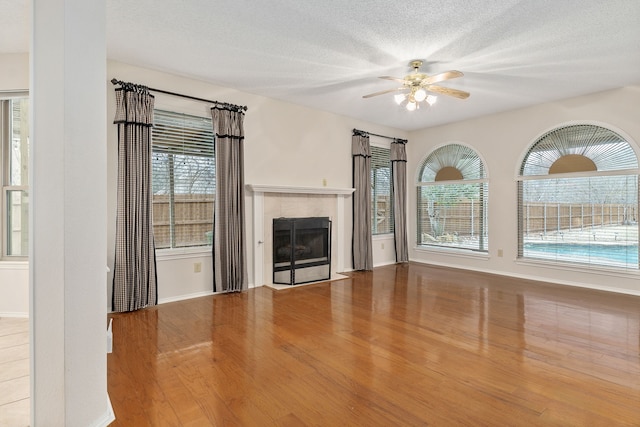 unfurnished living room featuring a tile fireplace, ceiling fan, a textured ceiling, and light hardwood / wood-style floors