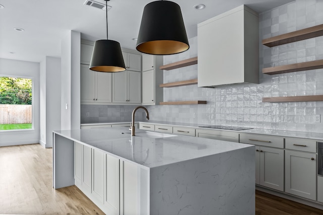 kitchen with pendant lighting, sink, black electric stovetop, light stone countertops, and light hardwood / wood-style flooring