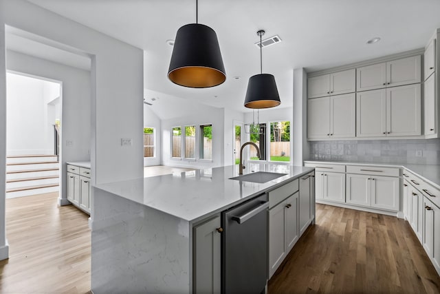 kitchen with sink, decorative backsplash, a kitchen island with sink, stainless steel dishwasher, and light stone countertops