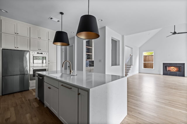 kitchen with pendant lighting, refrigerator, sink, a kitchen island with sink, and ceiling fan