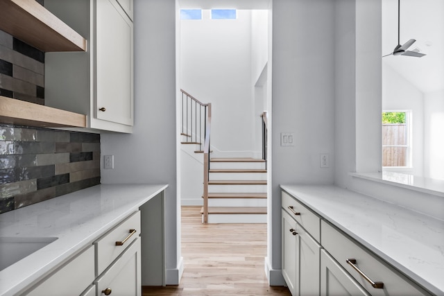 kitchen featuring vaulted ceiling, ceiling fan, light stone countertops, light hardwood / wood-style floors, and decorative backsplash