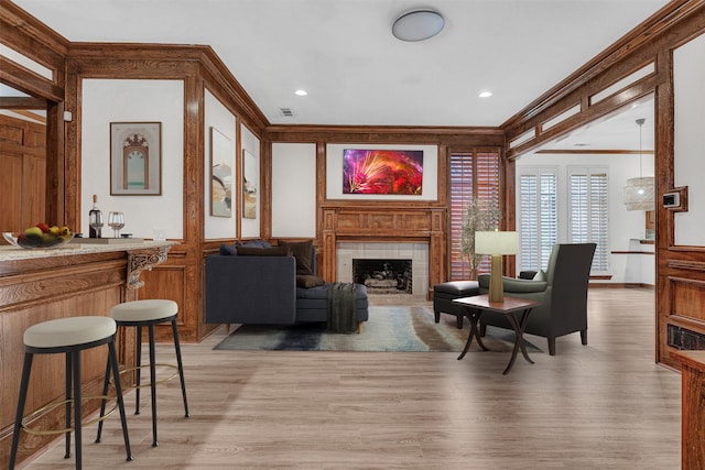 living room featuring visible vents, light wood-style floors, a dry bar, a tiled fireplace, and crown molding