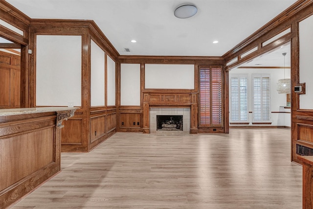 living room featuring crown molding, a fireplace, visible vents, a decorative wall, and light wood-style floors