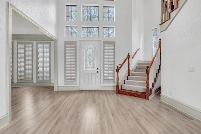 entryway with a towering ceiling, baseboards, stairway, and wood finished floors