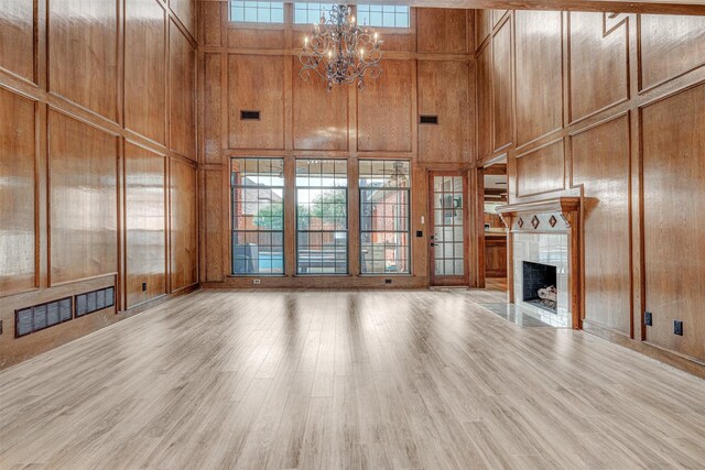 unfurnished living room with wood walls, light hardwood / wood-style floors, a tile fireplace, and a high ceiling