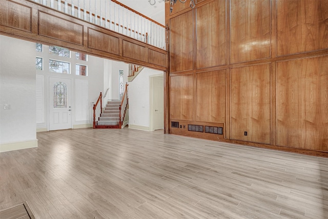 unfurnished living room featuring a towering ceiling, wooden walls, and light hardwood / wood-style flooring