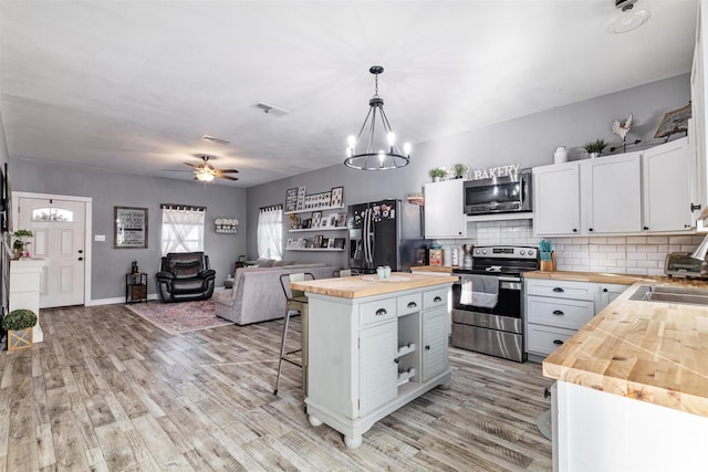 kitchen featuring pendant lighting, a breakfast bar area, appliances with stainless steel finishes, butcher block counters, and white cabinets