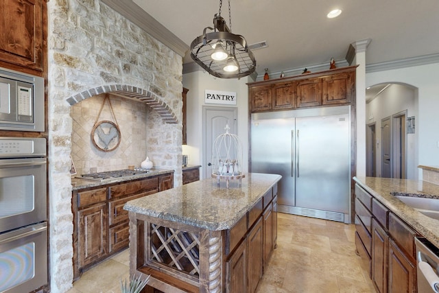 kitchen with light stone counters, arched walkways, backsplash, ornamental molding, and built in appliances