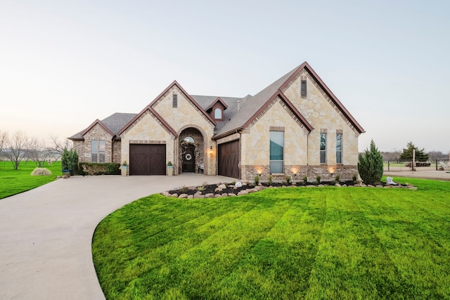 french country inspired facade featuring a garage, brick siding, concrete driveway, stone siding, and a front lawn