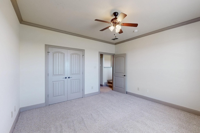 unfurnished bedroom featuring carpet floors, crown molding, a closet, visible vents, and baseboards