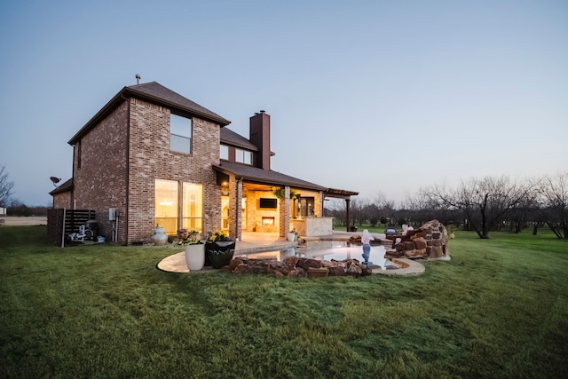 back of property featuring a chimney, a lawn, a patio, and brick siding