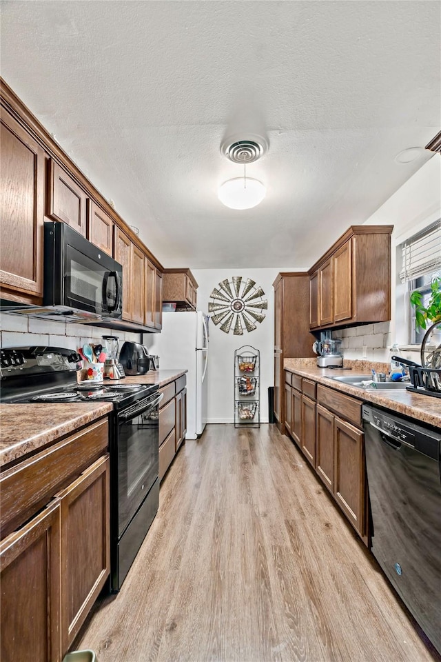 kitchen with tasteful backsplash, light hardwood / wood-style flooring, black appliances, and a textured ceiling