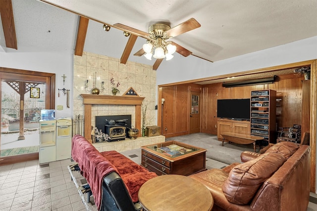 tiled living room with ceiling fan, vaulted ceiling with beams, wood walls, a textured ceiling, and a wood stove