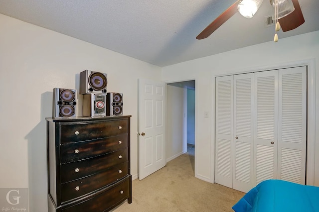 bedroom featuring ceiling fan, light carpet, a closet, and a textured ceiling