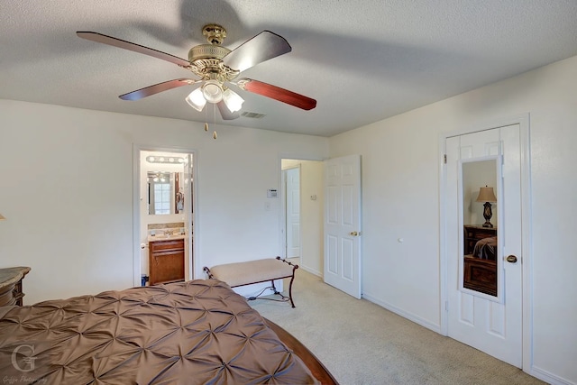 bedroom with ceiling fan, ensuite bathroom, light colored carpet, and a textured ceiling