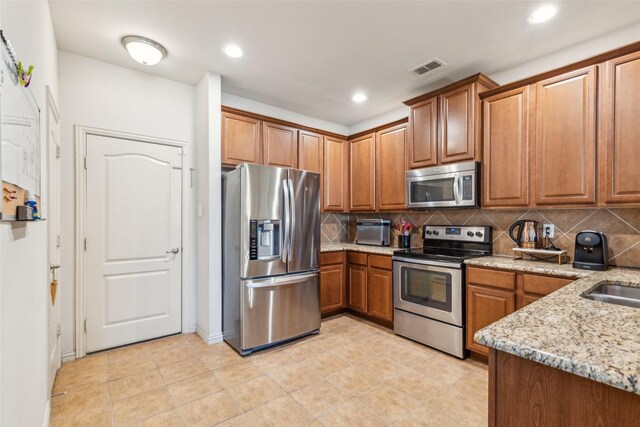 kitchen with sink, light stone counters, light tile patterned floors, appliances with stainless steel finishes, and decorative backsplash