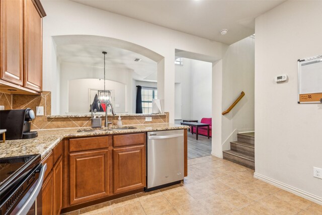 kitchen with appliances with stainless steel finishes, decorative light fixtures, tasteful backsplash, sink, and light stone counters