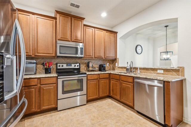 kitchen featuring pendant lighting, sink, appliances with stainless steel finishes, backsplash, and light stone countertops