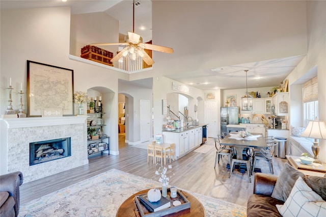 living room featuring sink, a high ceiling, a tiled fireplace, ceiling fan, and light hardwood / wood-style flooring