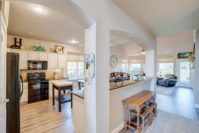 kitchen featuring lofted ceiling, tasteful backsplash, black appliances, white cabinets, and light wood-type flooring